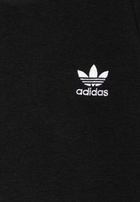 Fekete pamutszövet, melyen egy kis fehér Adidas-logó látható, három levél formájú díszítéssel a márkaneve felett, középen elhelyezve a ruhadarabon.