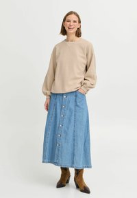 Sweatshirt beige oversize avec épaules tombantes, associé à une jupe en denim bleu clair avec un devant à boutons et des bottes à talons marron.