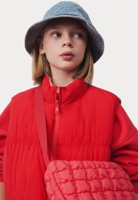 Rode puffer vest met hoge kraag en rits aan de voorkant, gecombineerd met een denim bucket hat en een gewatteerde rode crossbody tas. Gladde stoftextuur.