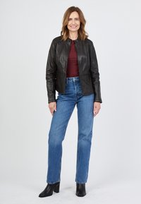 Sort læderjakke med en tætsiddende pasform, rund krave og subtil tekstur, parret med højtaljede blå jeans og sorte hælede ankelstøvler.