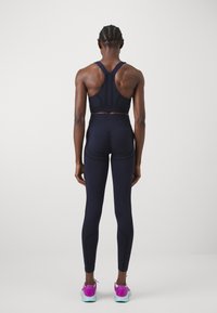 Top sportivo navy con design a schiena scoperta, leggings abbinati e sneakers a contrasto con dettagli rosa. Tessuto morbido e elasticizzato.