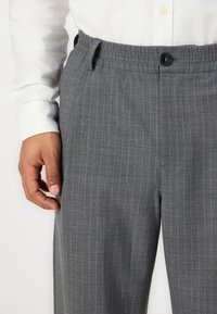 Gray pinstriped trousers featuring a button closure, elastic waistband, and a smooth fabric texture. Hand positioned at the side seam.