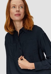 Dunkelblaues Hemd mit Knöpfen und strukturiertem Finish, ausgestattet mit zwei Brusttaschen und langen Ärmeln. Glattes Material und klassisches Kragen-Design.