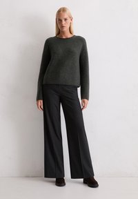 Dunkelgrauer, strukturierter Pullover mit langen Ärmeln, kombiniert mit weit geschnittenen, gestreiften Hosen und braunen Stiefeln. Schlichtes, modernes Design.