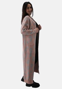 Cardigan lungo in morbido maglione rosa pallido, con stampa leopardata blu, due tasche frontali e polsini a coste. Indossato aperto, arriva a metà polpaccio.