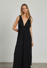 Vestido negro sin mangas con un profundo escote en V, cintura fruncida, tela fluida y detalles trenzados a lo largo de los lados, que cuenta con borlas ajustables.