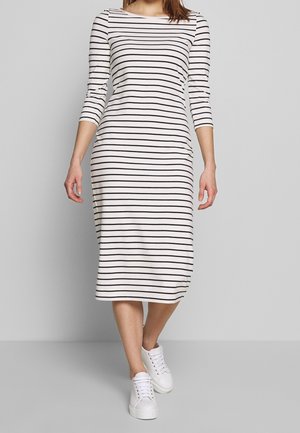 Kvinde iført en hvid midi-kjole med sorte vandrette striber og trekvartærmer, kombineret med hvide sneakers.