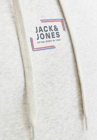 Sweat-shirt gris clair comportant un patch logo prominent avec « JACK & JONES » et l'année de création, avec des accents contrastants bleus et rouges.