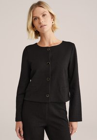 Černá croptop bunda vyrobená z texturované látky, s kulatým výstřihem, předními knoflíky se zlatými detaily a bočními kapsami.