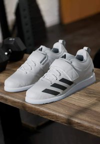 Białe buty sportowe z fakturowaną cholewką, z czarnym logo z trzema paskami, sznurowadłami i paskiem na śródstopiu. Gumowa podeszwa.