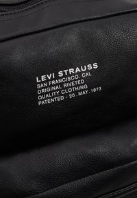 Tissu en cuir noir avec une surface texturée affichant du texte blanc, comprenant "Levi Strauss" et d'autres détails de la marque.