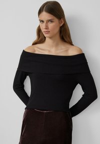 Schwarzes, schulterfreies, geripptes Oberteil mit langen �Ärmeln, das einen weiten Ausschnitt und eine enge Silhouette aufweist, kombiniert mit dunklem, strukturiertem Stoff darunter.