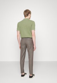Polo vert à manches courtes, associé à un pantalon marron sur mesure et des baskets noires, vu de dos. Design simple et épuré, tissu texturé.