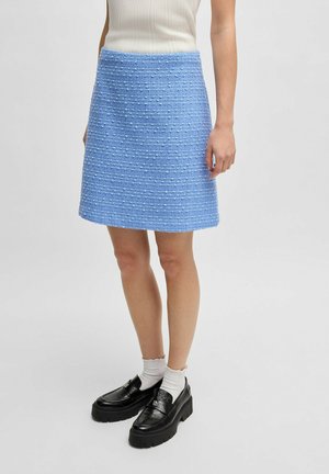 Blauwe tweed rok met gestructureerde strepen, boven de knie lengte, aangevuld met zwarte platte loafers en witte geribbelde sokken.