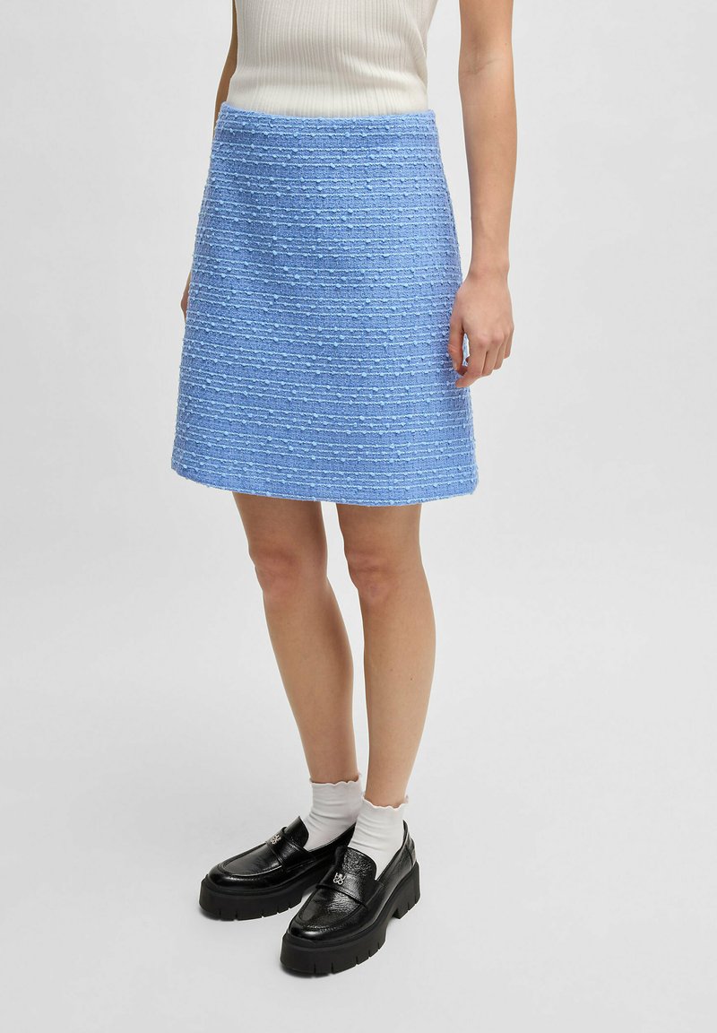Blauwe tweed rok met gestructureerde strepen, boven de knie lengte, aangevuld met zwarte platte loafers en witte geribbelde sokken.