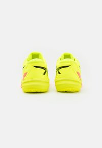 Zapatillas deportivas de color amarillo brillante con acentos negros, suela texturizada y detalles en rosa. Presentan un diseño de perfil bajo y un collar acolchado.