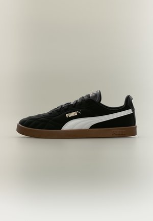 Μαύρο αθλητικό παπούτσι Puma με λευκή πλευρική λωρίδα και καφέ σόλα, προβεβλημένο σε προφίλ πάνω σε απλό ανοιχτό φόντο.