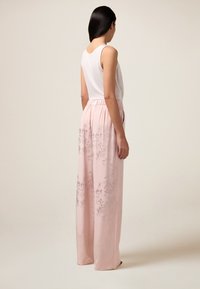 Light pink wide-leg pants with a soft texture, featuring a subtle floral pattern. Paired with a white sleeveless top, visible elastic waistband.