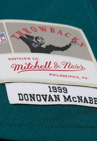 Türkisfarbener Trikot mit Mesh-Struktur, versehen mit einem Etikett, das "Throwbacks", "Mitchell & Ness" und "1999 DONOVAN MCNABB" in kontrastierenden Farben zeigt.