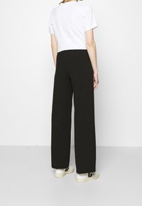 Sorte vide benbukser lavet af et glat stof, med høj talje og blød tekstur. Sættes sammen med en hvid kortærmet skjorte og sneakers.