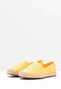 Espadrilles en toile jaune avec une semelle en jute tissée, mettant en avant des détails brodés sur le bout et un design sans lacets.