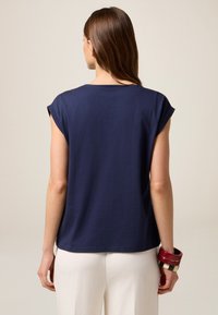 Top de manga corta azul marino con un corte relajado, escote redondeado y textura suave, combinado con pantalones blancos y pulseras en capas.