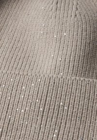 Tessuto a maglia a costine beige con una superficie testurizzata, decorato con piccole paillettes argento sparse per un ulteriore dettaglio e interesse visivo.