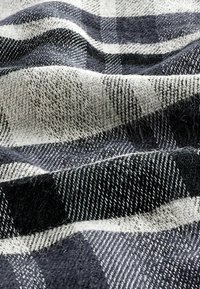 Kariertes Gewebe in Schwarz- und Grautönen mit einer weichen, strukturierten Webart. Helle und dunkle Quadrate bilden ein kontrastierendes Muster.