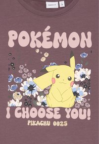 Maglietta di cotone viola con una grafica di Pikachu gialla circondata da fiori colorati, con il testo audace "POKÉMON TI SCEGLIO IO!" e dettagli glitterati.