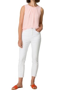 Top sin mangas de color rosa claro con pliegues, combinado con jeans blancos cortos y sandalias naranjas, mostrando un atuendo casual y veraniego.