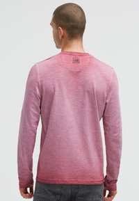 Long-sleeve shirt in gradient pink, soft texture, crew neckline, and tag on the back neck. Features smooth seams and a relaxed fit.