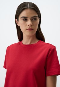 T-shirt in cotone rosso con scollo rotondo e maniche corte. Texture liscia, senza motivi visibili, design semplice e classico.