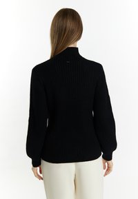 Maglione nero a coste con collo alto e maniche a palloncino, caratterizzato da una vita aderente, una consistenza morbida e un design minimalista.