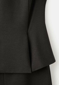 Haut peplum noir en tissu texturé, présenté avec un design structuré, un ourlet évasé et une finition lisse. Sans quincaillerie ni accents visibles.