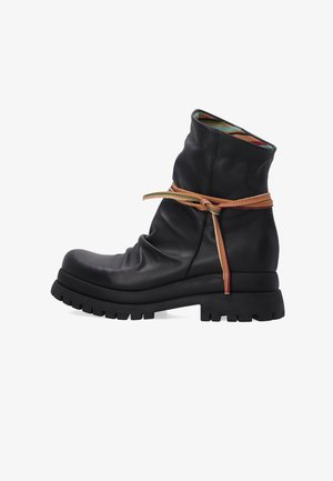 Czarne skórzane botki za kostkę o luźnym kroju, z gumową podeszwą i wplecionymi akcentami w kolorze tan. Kolorowa podszewka jest częściowo widoczna.