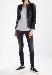 Černá kožená bunda, šedý svetr s výstřihem do V, slim džíny tmavé barvy, černé slip-on boty. Hladký materiál s přiléhavým střihem a rukávem svetr s žebrovaným lemem.