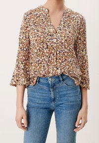 Brun blomster skjorte med v-hals, trekvart ærmer, en løs pasform, og en blanding af hvide, gule, orange og blå mønstre bæret med blå jeans.