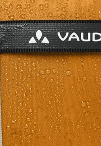 Tejido impermeable en color naranja con un acabado texturizado, que presenta una correa negra con la marca "VAUDE" en blanco y gotas de agua.