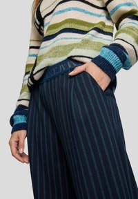 Gestrickter Pullover mit grünen, blauen und marinefarbenen Streifen; marinefarbene gestreifte Hose mit strukturierter Bundpassform. Mitellange Ärmel und sichtbare Fronttasche.