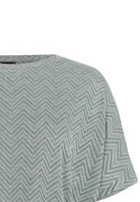 Haut à manches courtes avec un motif en zigzag vert clair et gris, col rond, visible de la partie supérieure de la poitrine à l'épaule.