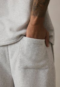 Hellgrauer, strukturierten Stoff mit einer weichen Oberfläche, der eine seitliche Tasche zeigt. Das Kleidungsstück ist tailliert und hat ein Kurzarmdesign.