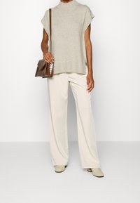 Pull sans manches en tricot beige avec un col montant, associé à un pantalon large crème et un sac à main en cuir d'agneau marron.