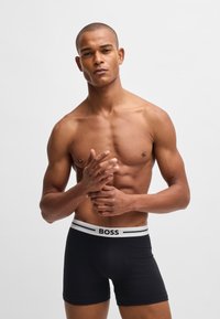 Black boxer briefs with a white waistband featuring the text "BOSS." Smooth fabric with a snug fit and short leg length. No patterns or hardware.