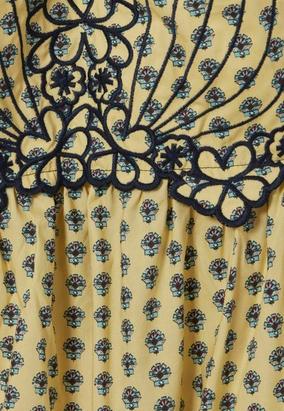 Tessuto giallo con un motivo floreale blu e rosso. Un dettaglio ricamato nero sul colletto aggiunge texture e un accento decorativo.