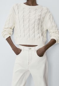 Pull en tricot blanc avec un motif en côtes, design court et manches larges ; associé à un jean blanc taille haute avec poches latérales.