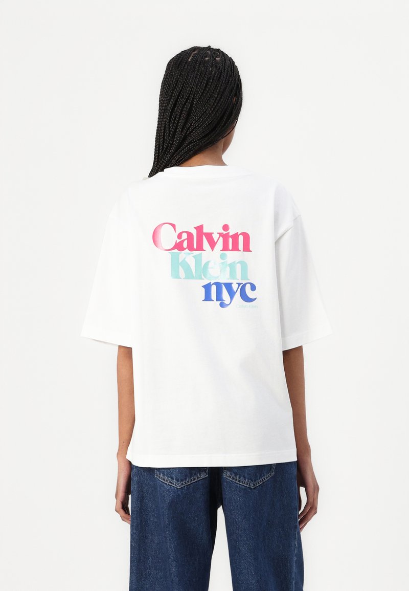 Balta per didelė T-marškiniai su daugiaspalviu tekstu: "Calvin Klein nyc" rožinės, žydros ir mėlynos spalvų. Apvalus iškirpimas, trumpomis rankovėmis, laisvas prsitaisymas.