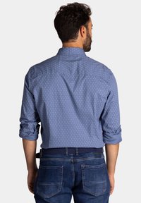 Lichtblauw overhemdshem met kleine witte patronen, opgerolde mouwen en een klassieke kraag, gecombineerd met donkerblauwe denim jeans.