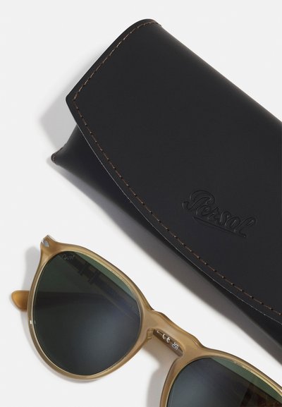Ochelari de soare cu tortoiseshell maro, dotati cu lentile de culoare verde închis, având o marcă subtilă. Include o husă din piele neagră cu cusături maro.