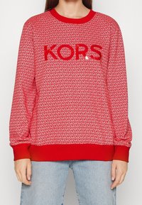 Felpa rossa con logo ripetuto, collo rotondo e polsini a costine. Il testo lucido "KORS" è ben visibile sul davanti.
