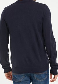 Pull bleu marine à manches longues avec un col rond, des poignets et un ourlet côtelés, fabriqué en tissu tricoté doux, porté avec un jean denim bleu clair.